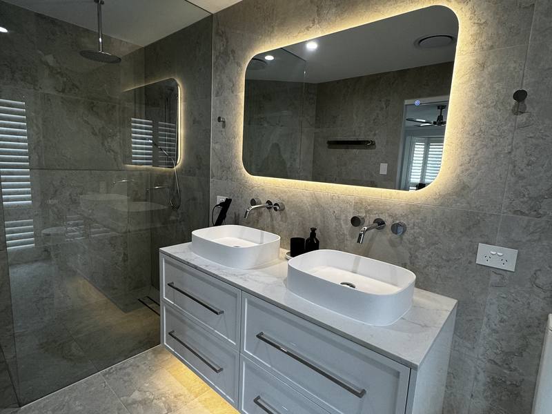 Renovated bathroom with twin basins, backlit mirror and travertine walls