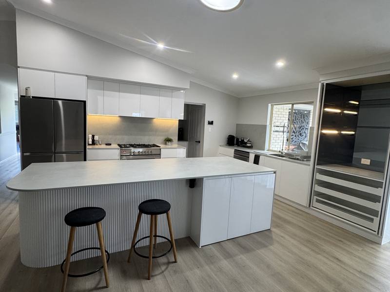 Open plan white kitchen with a curved fluted island and timber flooring