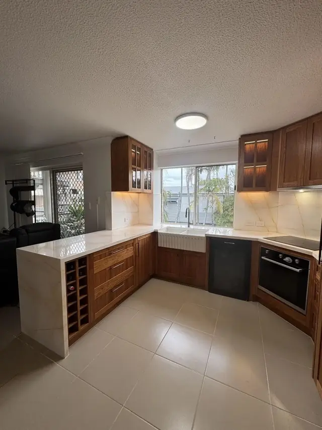 Kitchen with timber cabinetry, marble-look stone benchtops with a waterfall end, a farmhouse sink under the window and a built-in wine rack