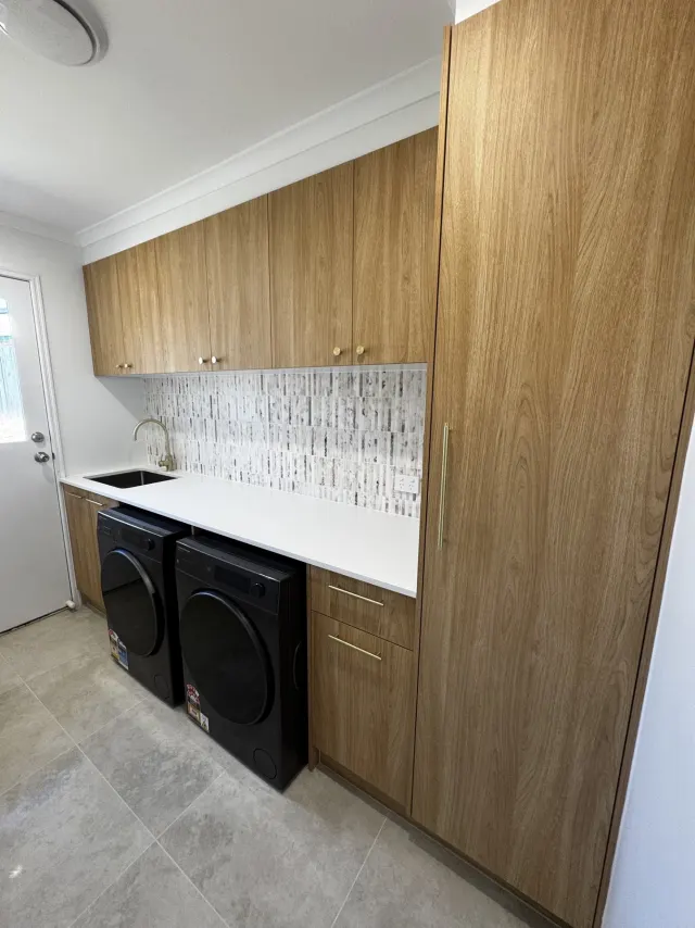 Renovated Regents Park laundry with timber-look cabinetry, overhead storage, white benchtop and side-by-side appliances