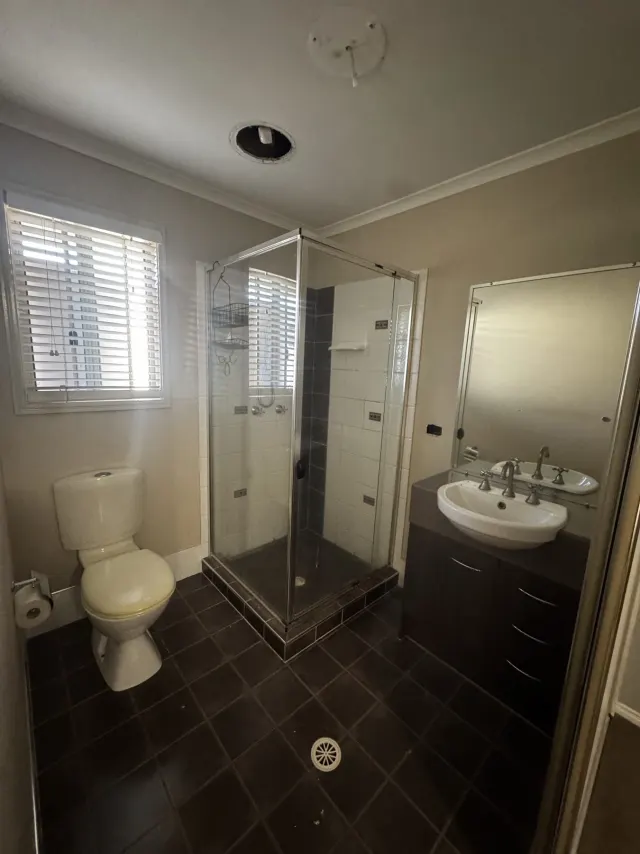 Before: the original Regents Park shower and vanity, with a framed glass screen, a rectangular mirror and dark floor tiles