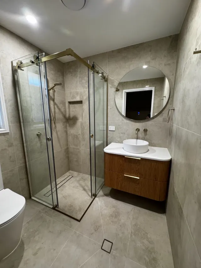 After: the same Regents Park shower and vanity, with a glass enclosure, a recessed shelf, a wall-hung fluted timber-look vanity and a round mirror