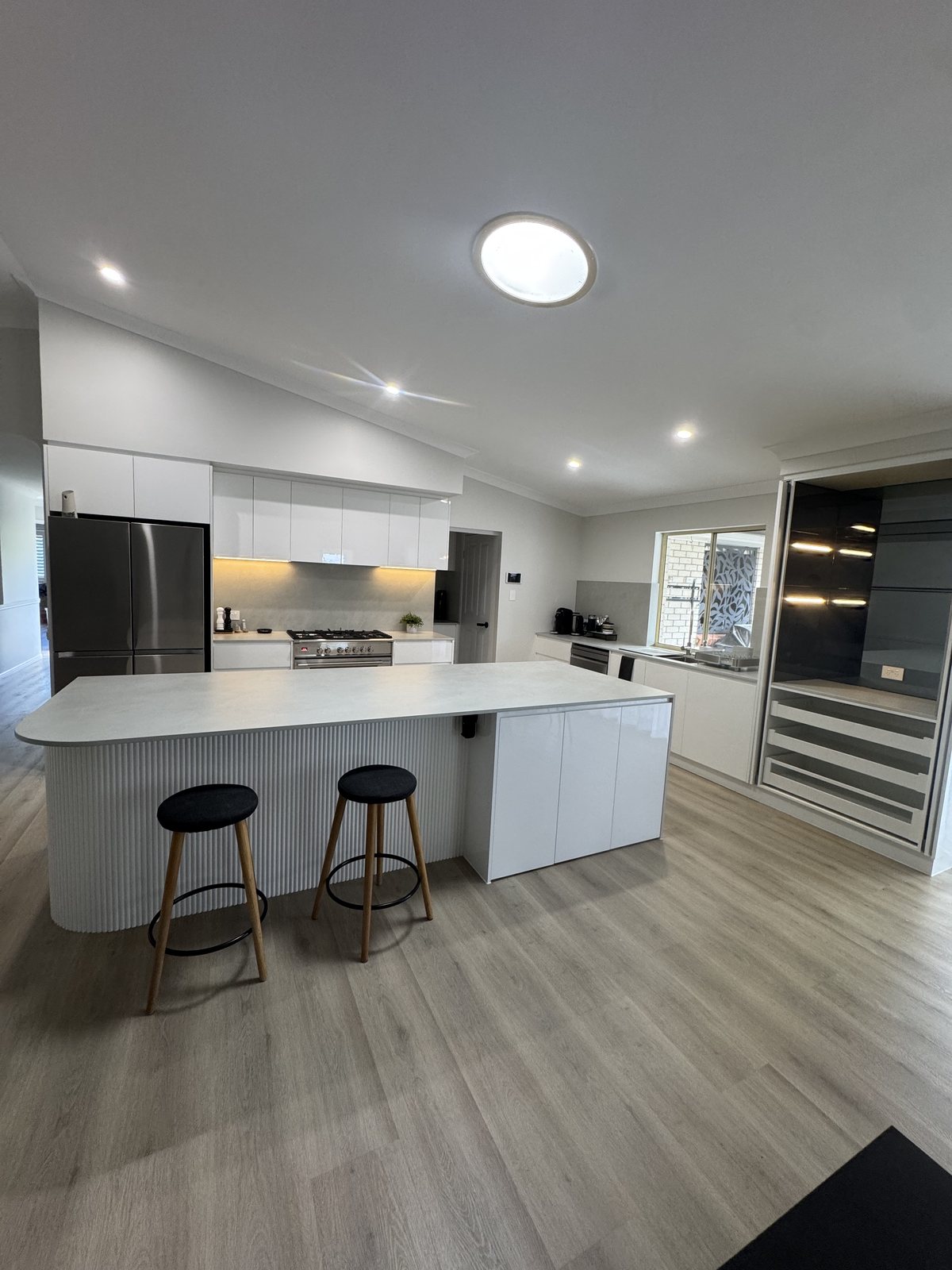 Kitchen island with bar stools, fridge recess and pantry beyond