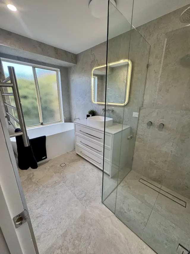 The Wellington Point main bathroom, with a freestanding bath under the window and a walk-in shower alongside