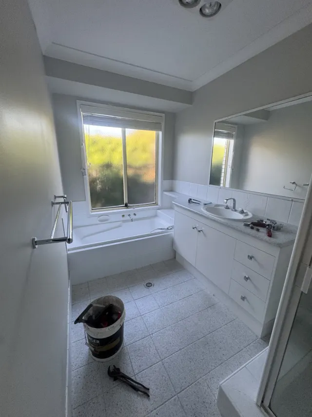 Before: the original Wellington Point main bathroom, with a bath under the window, a dated vanity and speckled tile