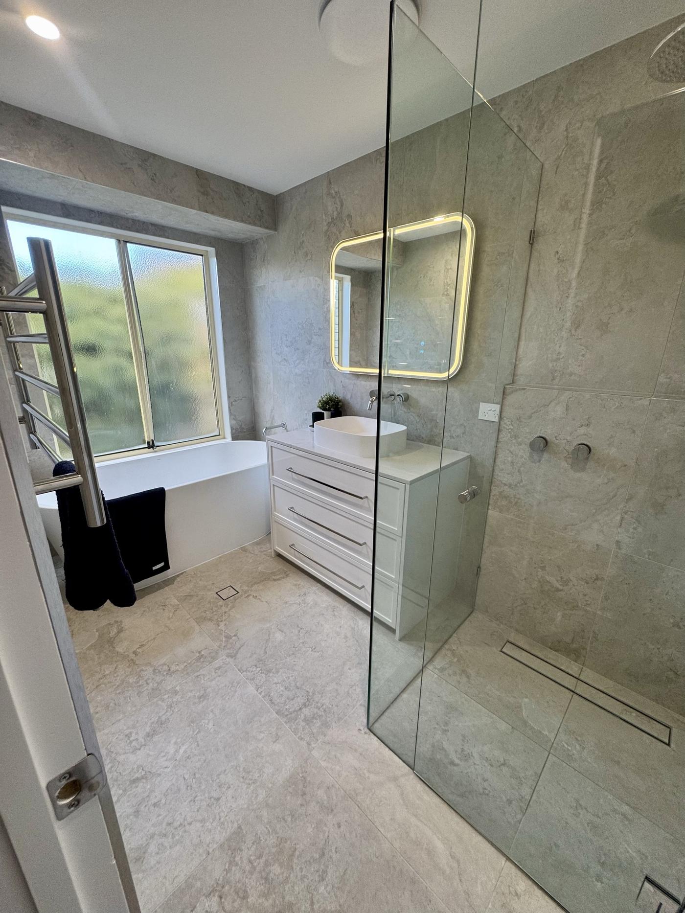 Freestanding bath under a window with walk-in shower alongside