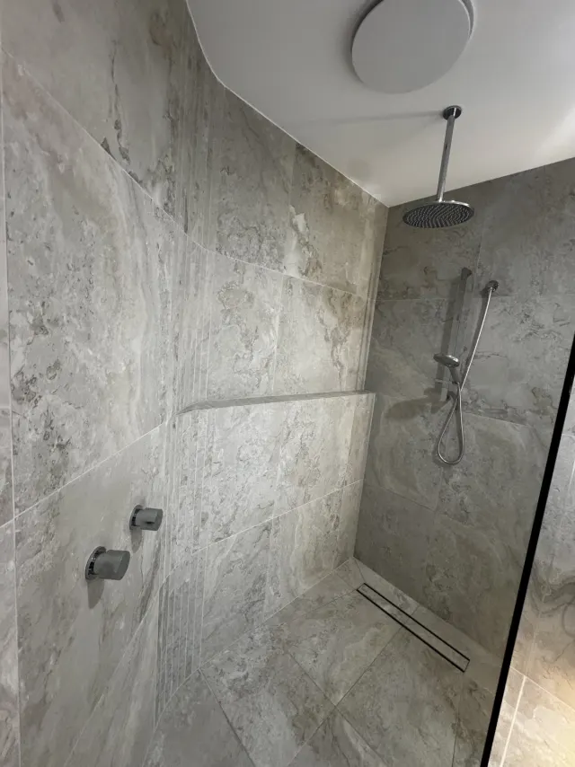 Walk-in shower with rain head, hand shower and linear floor drain in travertine