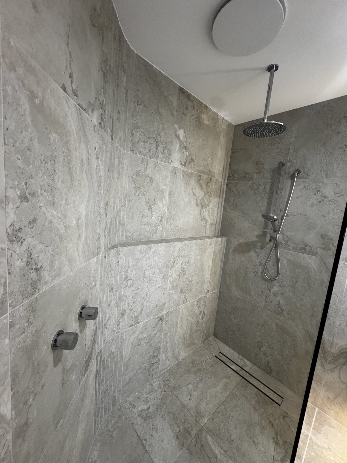 Walk-in shower with rain head, hand shower and linear floor drain in travertine