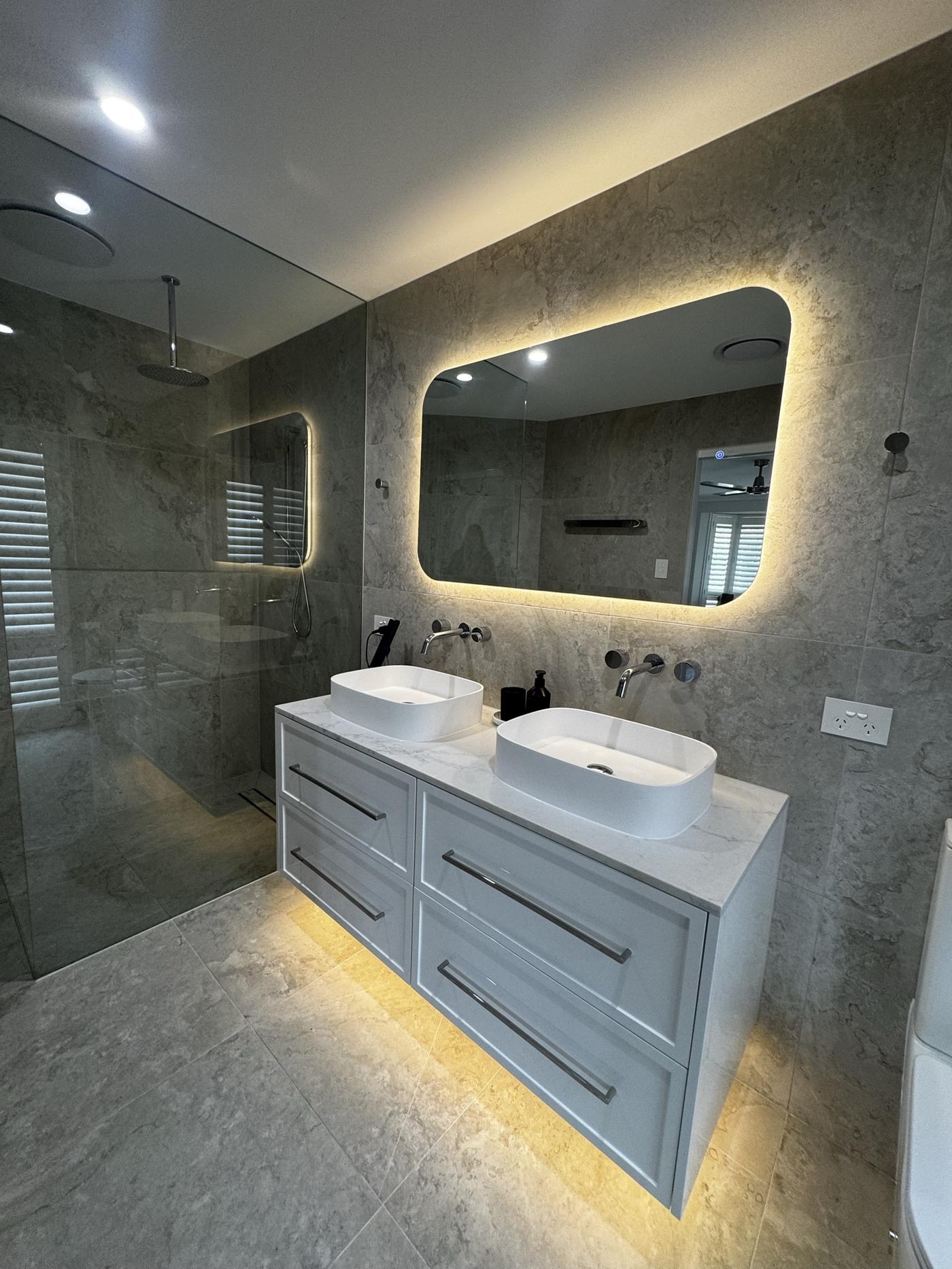 Double vanity with twin basins, backlit mirror and travertine walls
