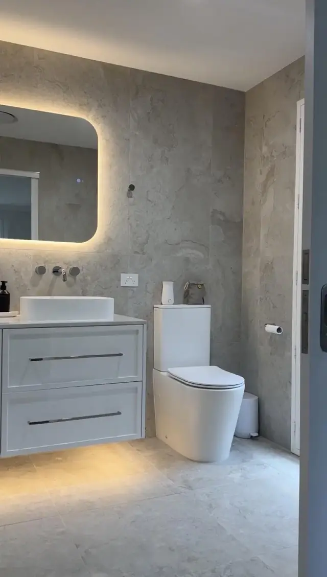 Vanity and backlit mirror with travertine wall tile