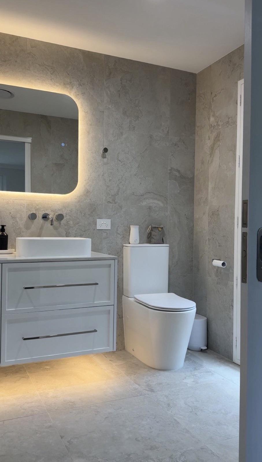 Vanity and backlit mirror with travertine wall tile